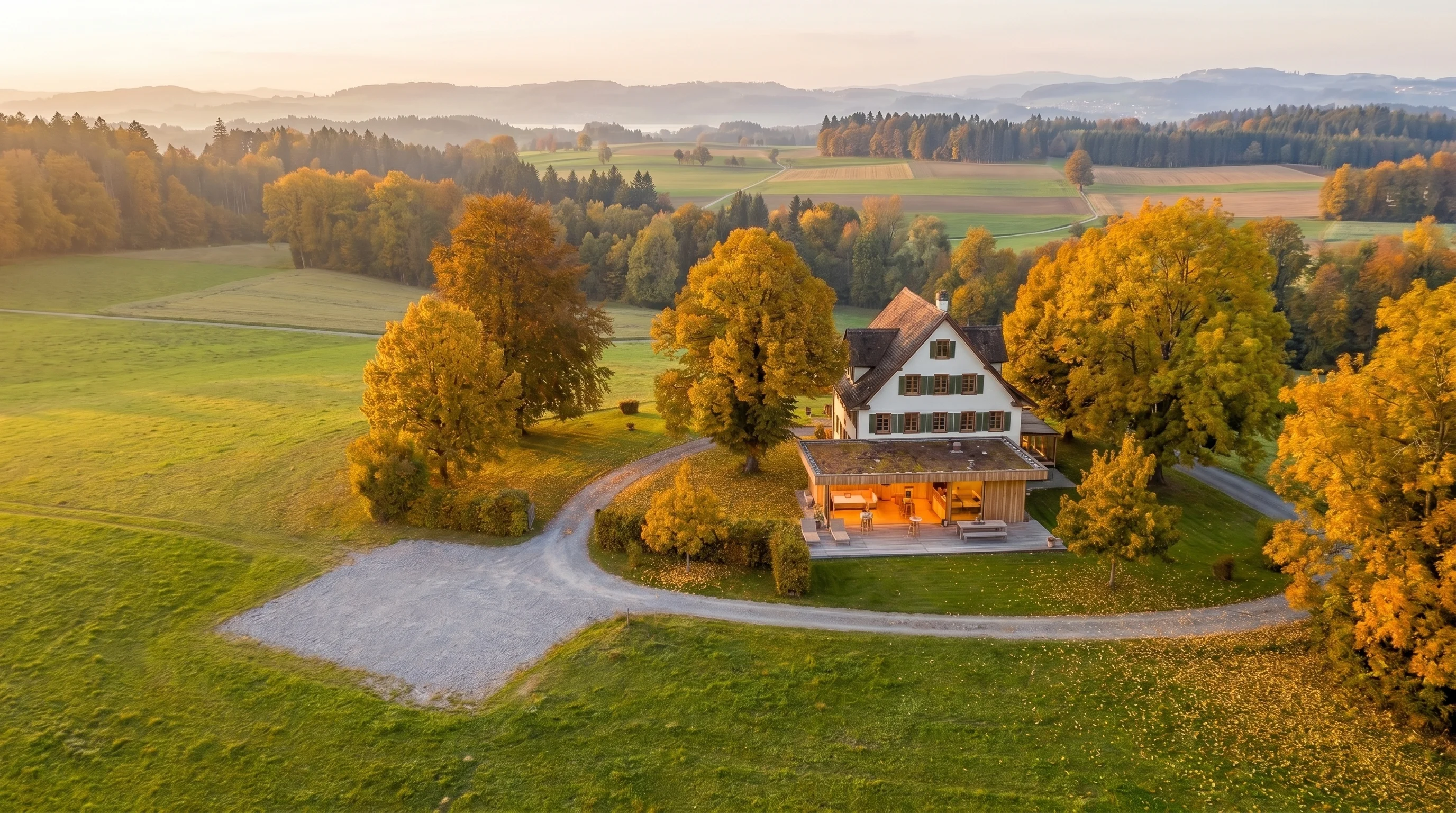 Das Landhaus Sihlweid im Herbst — Bauernhaus und Glaspavillon auf einer Lichtung, umgeben von bunten Laubbäumen.