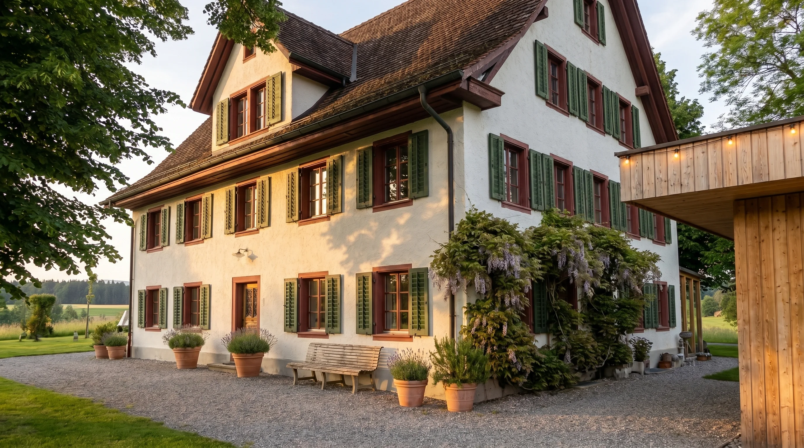 Das historische Landhaus im späten Nachmittagslicht — weiss verputzte Fassade mit grünen Fensterläden, Lavendel im Vordergrund.