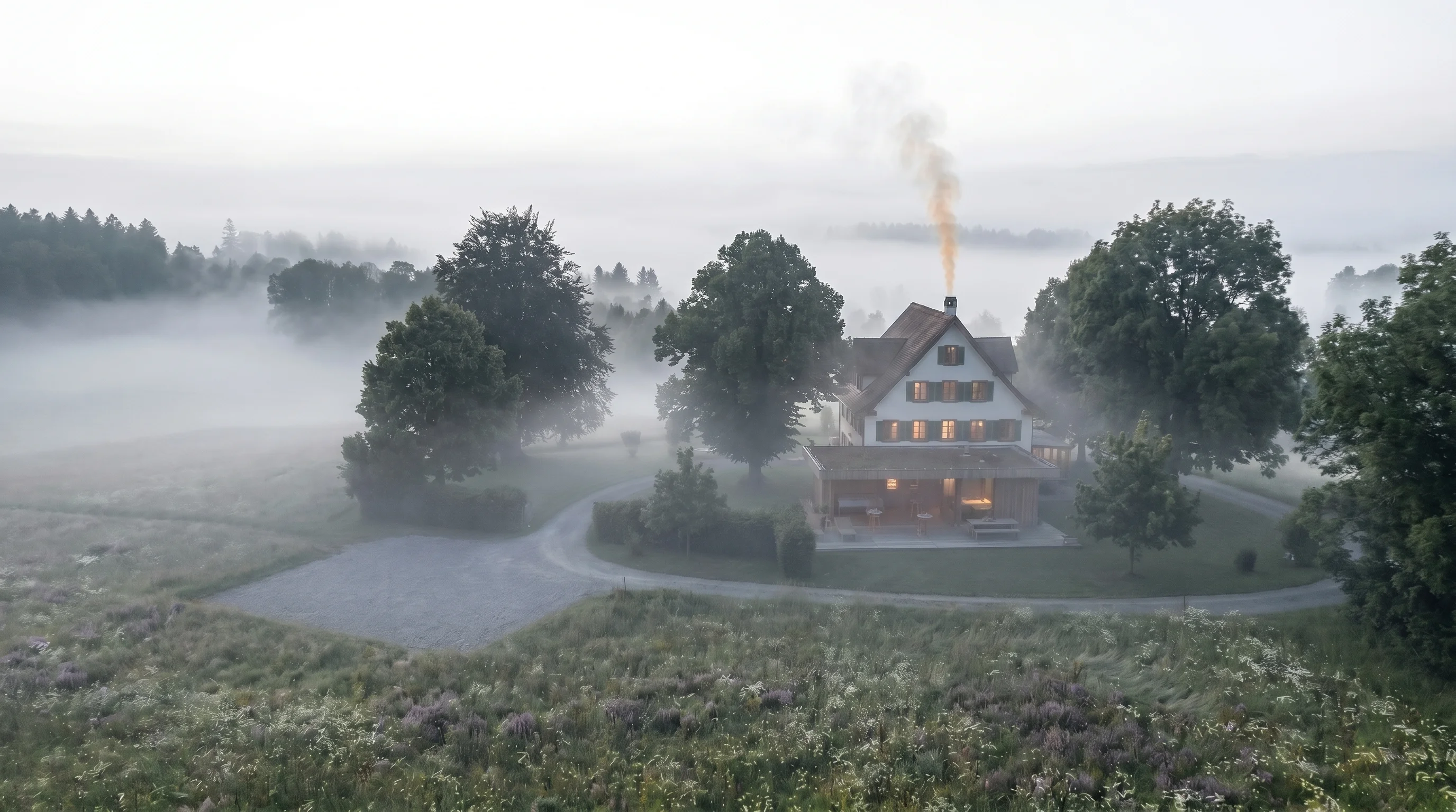 Morgennebel über dem Landhaus Sihlweid — Bauernhaus und Glaspavillon tauchen schemenhaft aus dem Nebel auf.