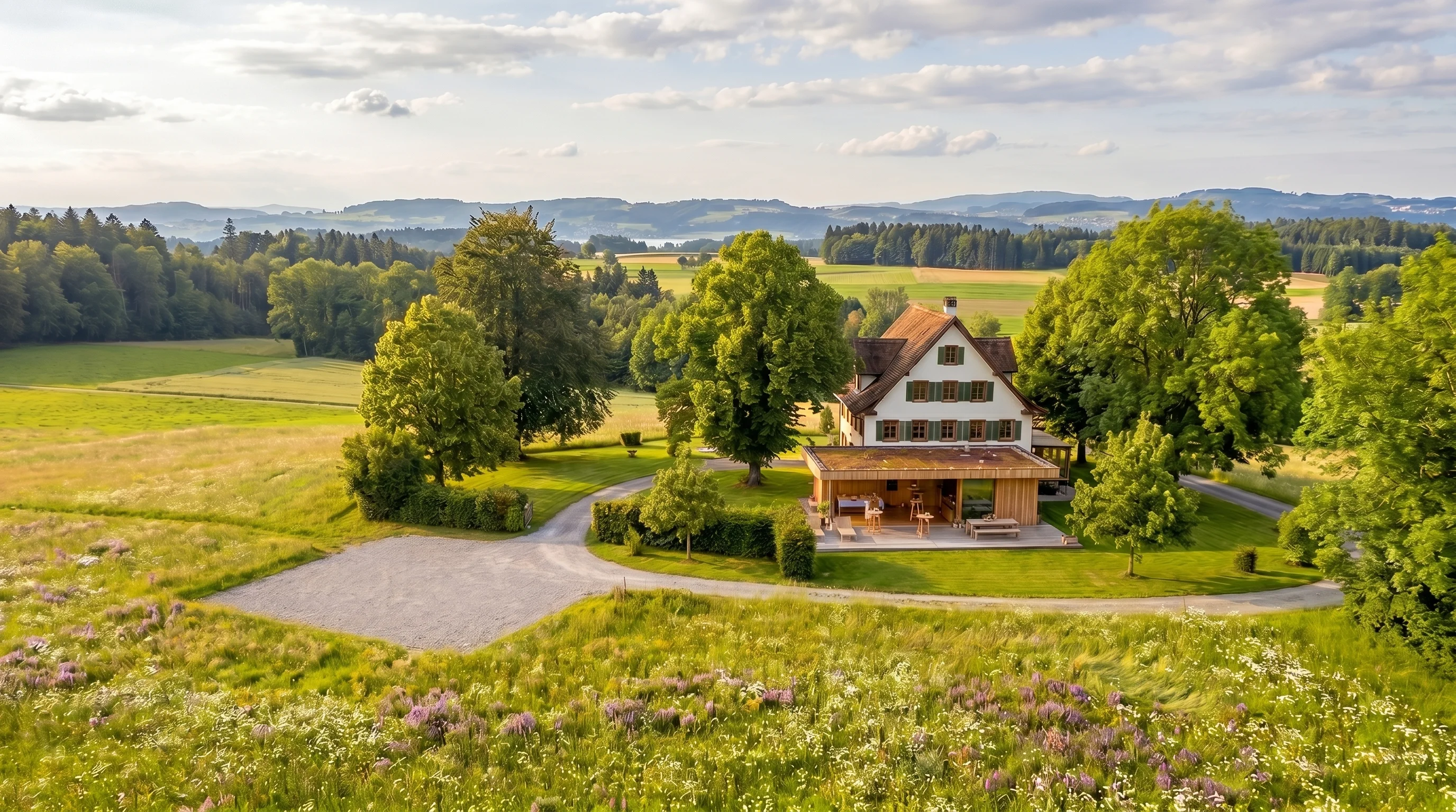 Landhaus Sihlweid im Sommer — warme Nachmittagssonne, blühende Wildblumenwiese, Waldrand im Hintergrund.