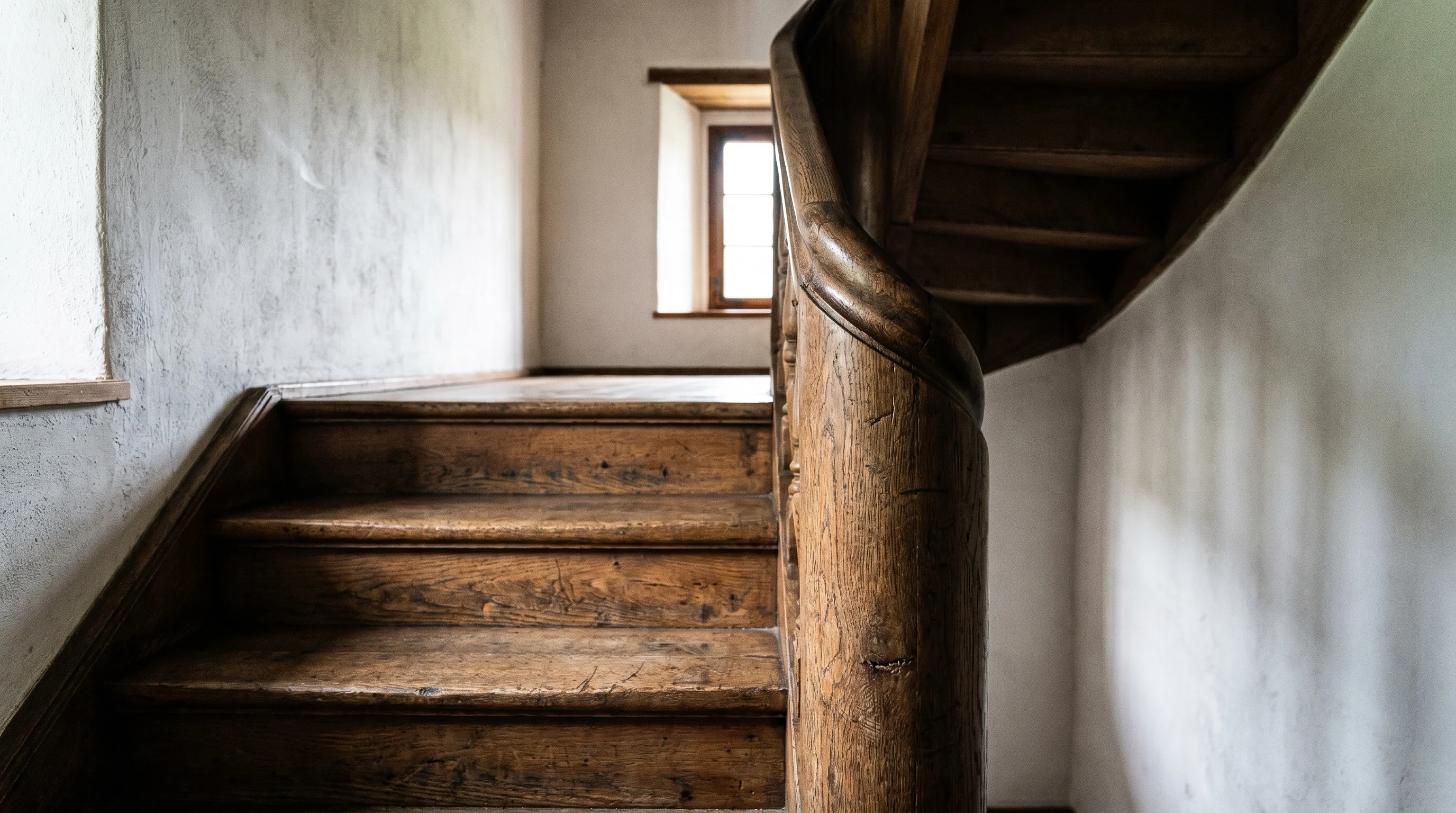 Historische Holztreppe im Landhaus — Detailansicht mit gedrechseltem Pfosten, weisser Kalkwand und seitlichem Tageslicht.